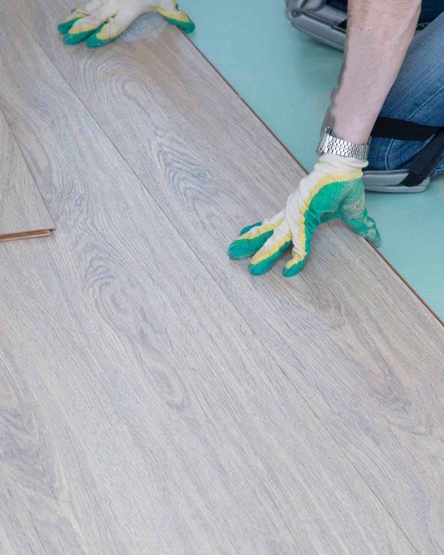 Installer laying light gray luxury vinyl plank (LVP) flooring